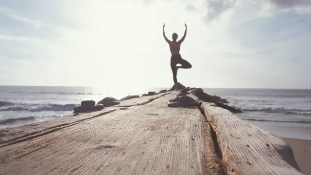 Frau in Yoga-Haltung am Ende eines Holzstegs am Meer